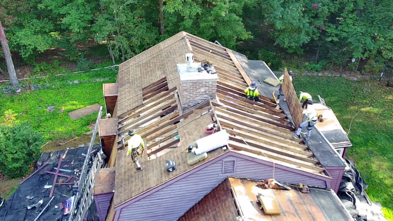 Aerial view of the Genesis crew mid-tear-off on a red house, exposed decking and chimney flashing