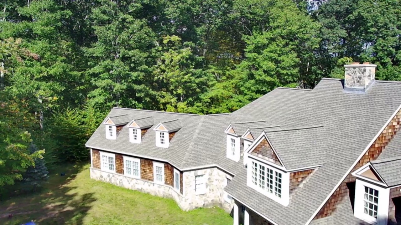 Aerial view of a dormered home with a new roof set in dense forest