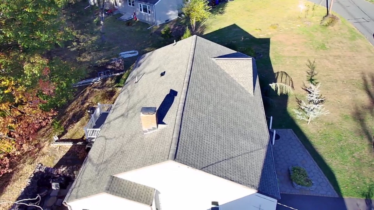 Aerial view of a finished shingle roof surrounded by fall foliage