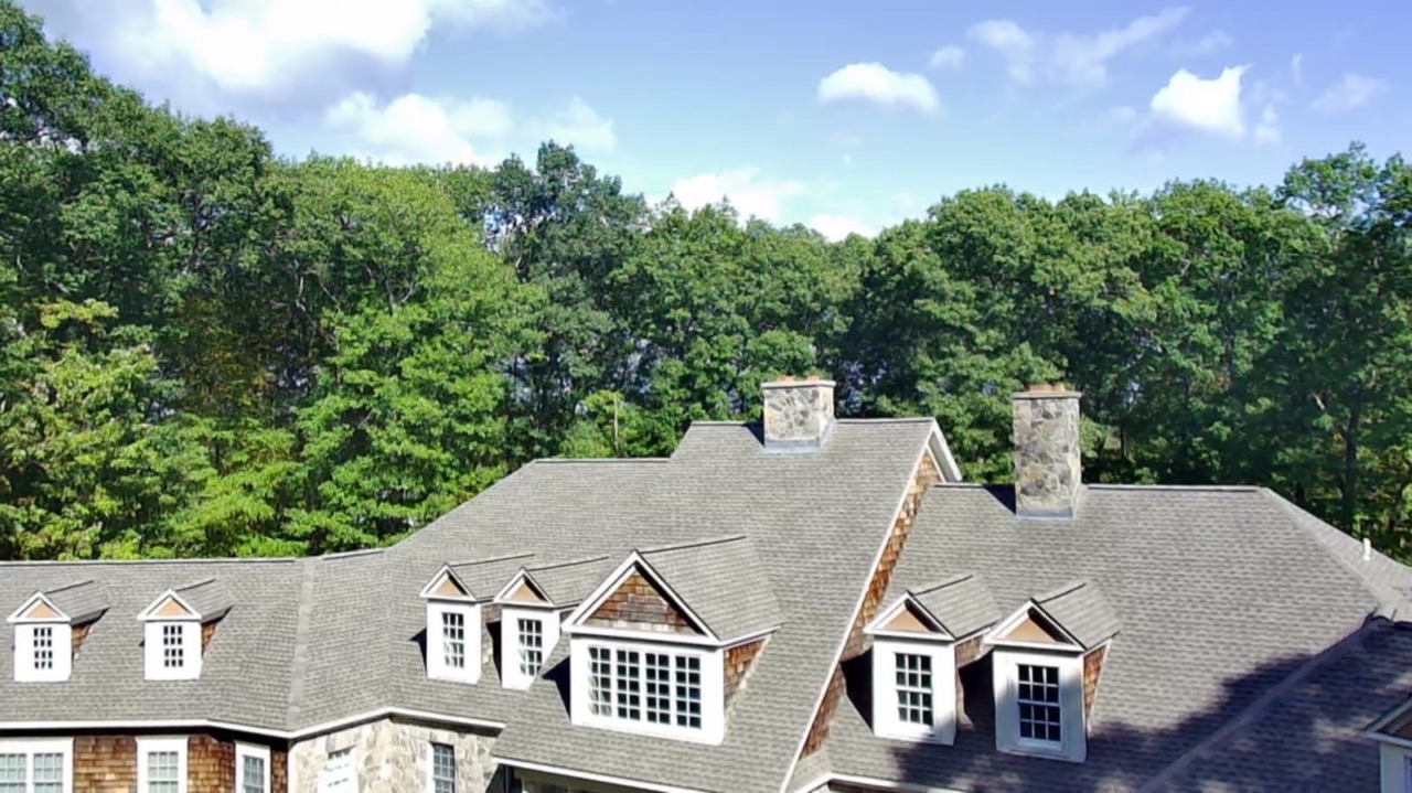 Aerial view of a large home with a finished roof surrounded by forest