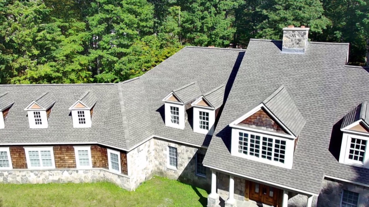 Aerial view of a large dormered home with a finished shingle roof