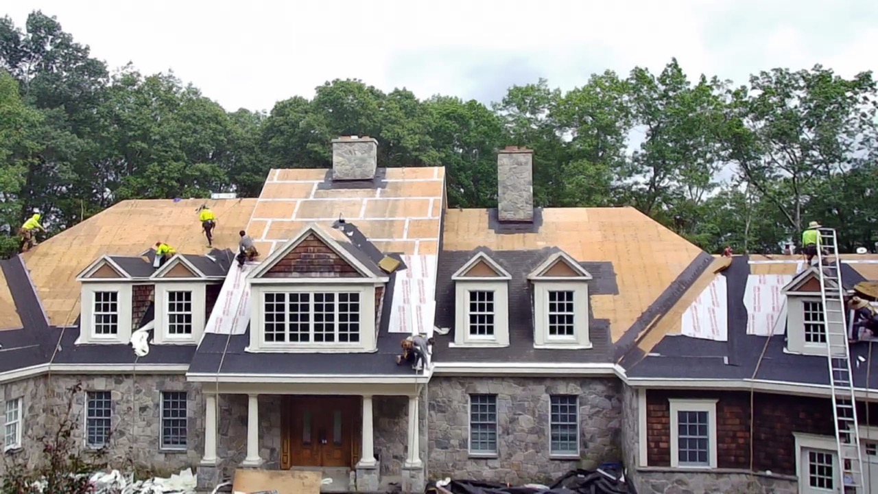 Aerial establishing shot of a large stone-and-shingle home with multiple dormers