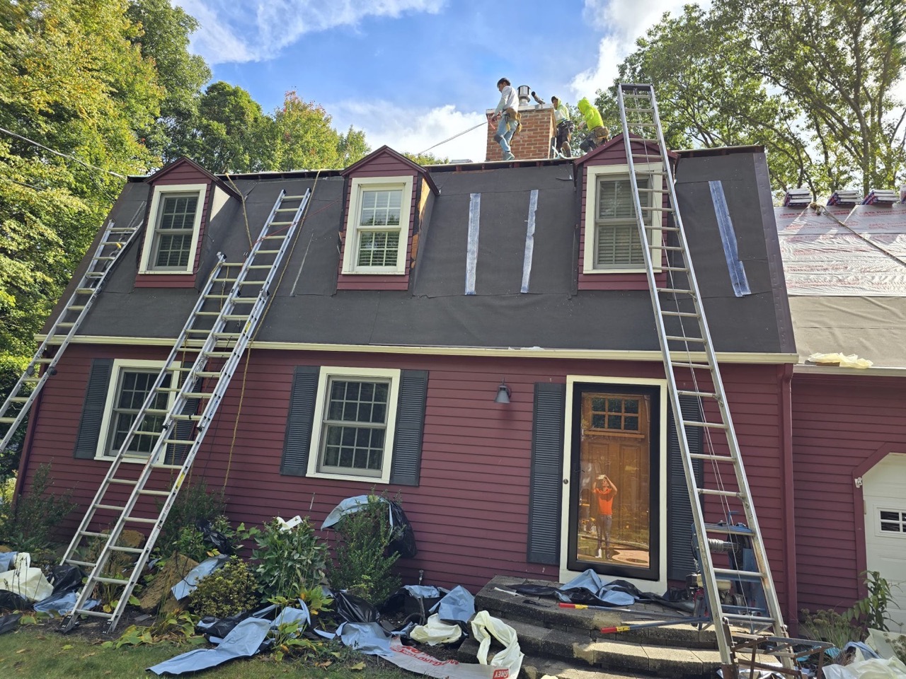 A ladder set against a colonial home mid-reroof, Genesis crew on site