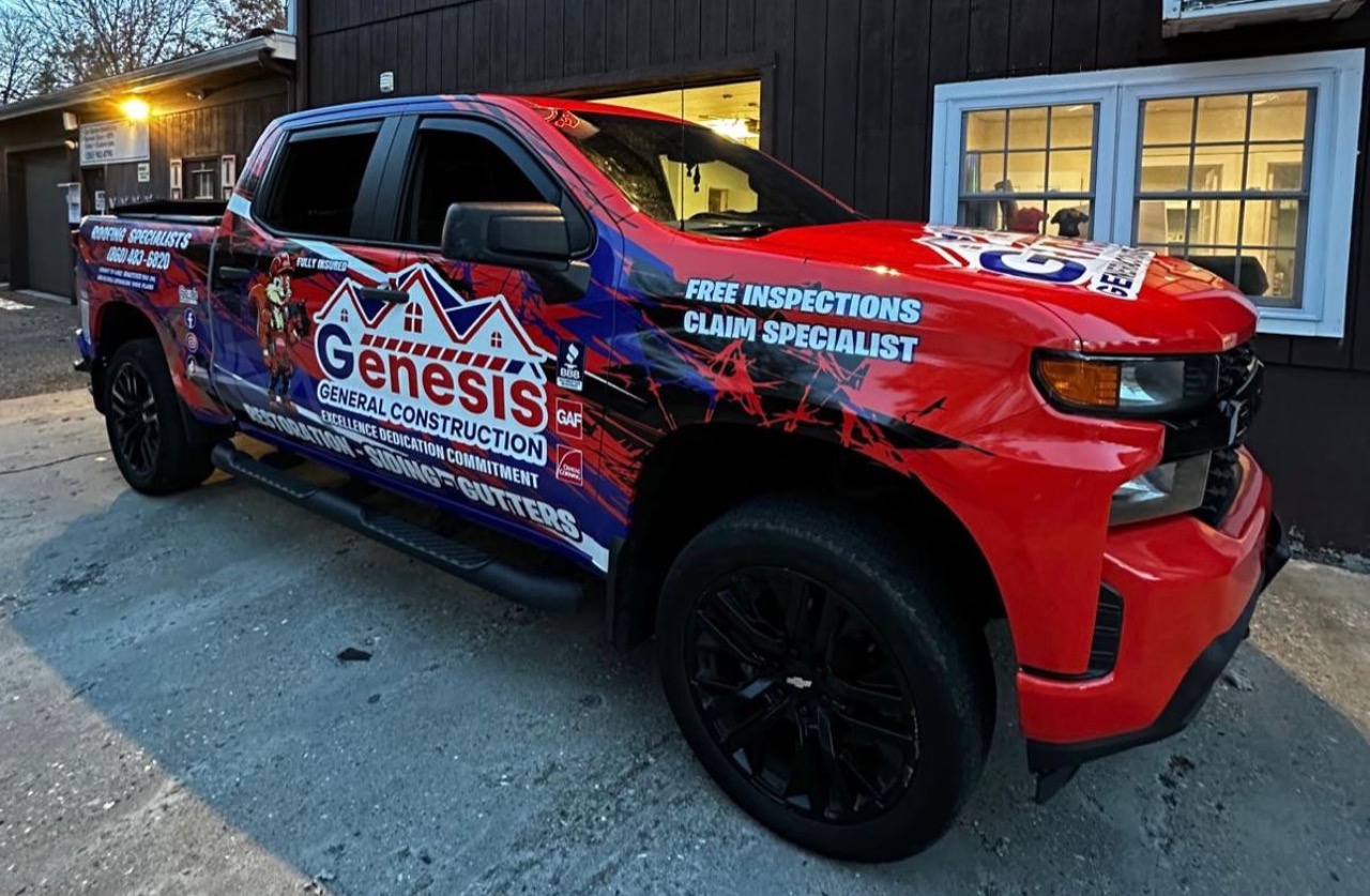 Genesis General Construction's fully wrapped company truck parked at dusk in front of their Waterbury shop, advertising Roofing Specialists, Free Inspections and Claim Specialist services